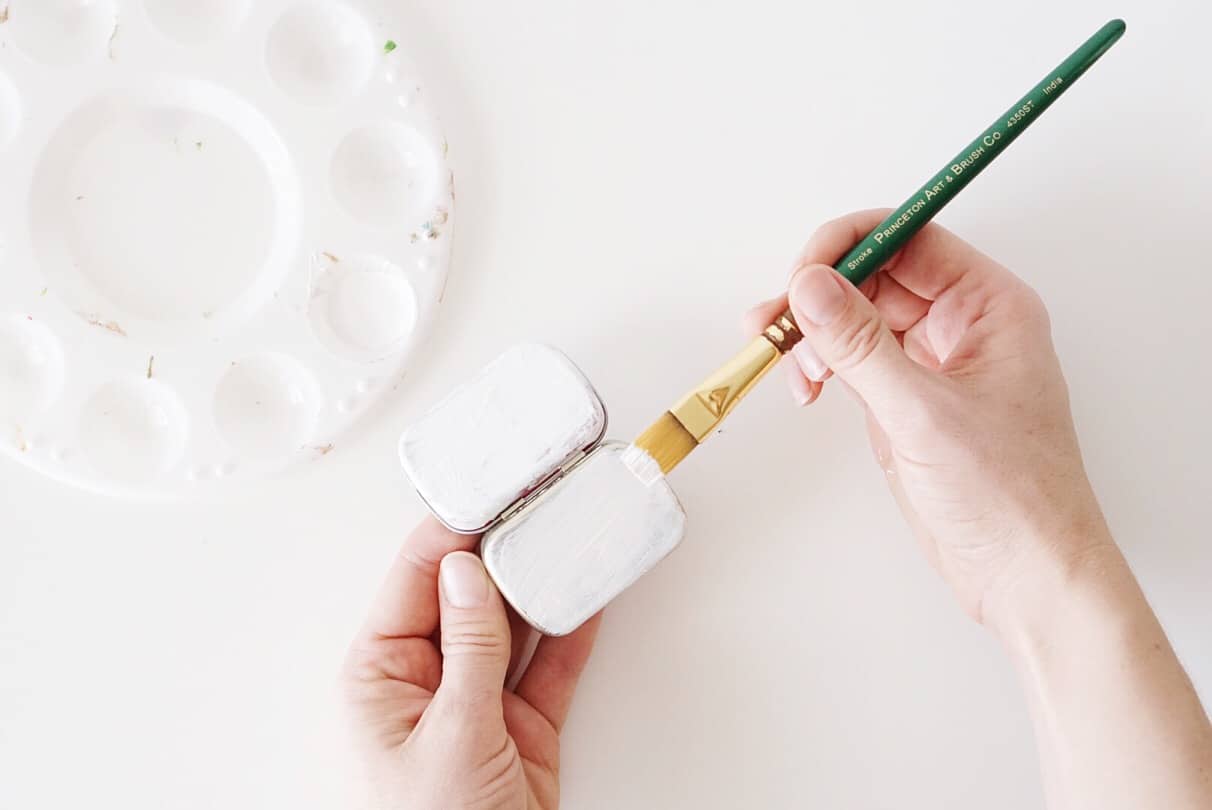Painting the bottom of a metal mint tin with white acrylic paint