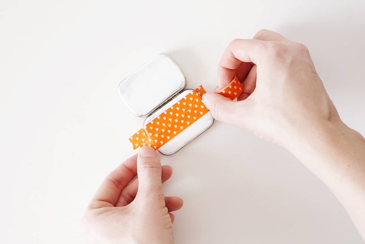 Hands adding the washi tape to the tin